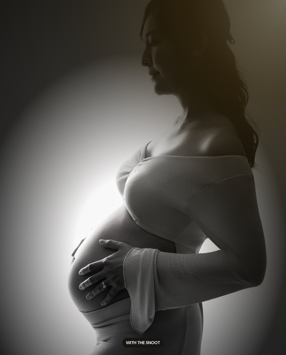 The same maternity portrait with a snoot spotlight, the room falling away to black around a pool of light